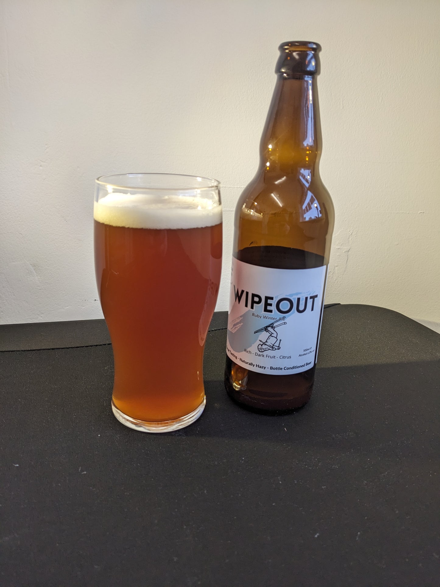 Beer poured into a pint glass with bottle beside it. Wipeout Ruby Ale. Great Tasting Naturally Hazy Bottle Conditioned Beer