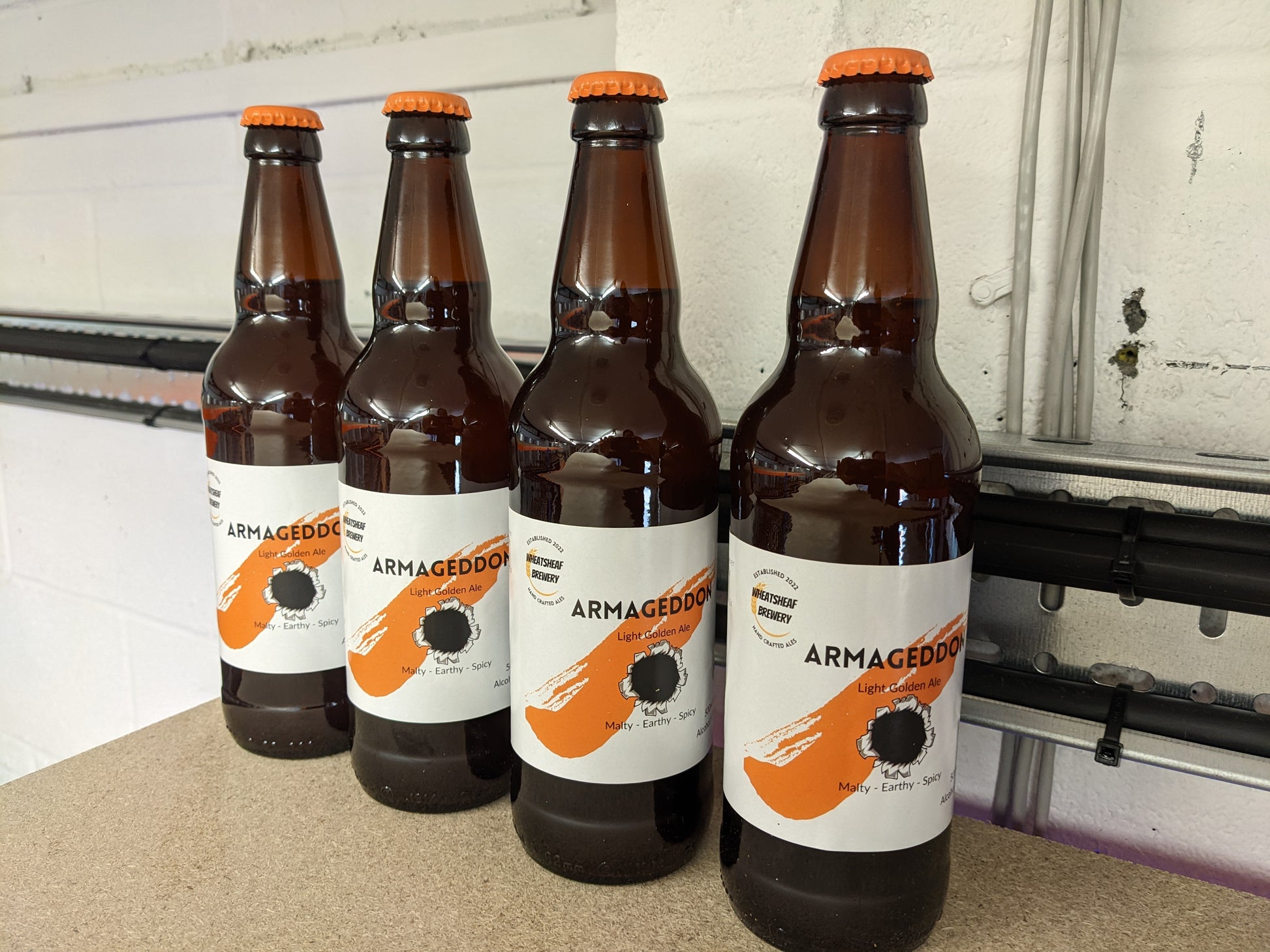 Four bottles of Armageddon golden ale on the shelf with orange caps. Bottle conditioned real ale brewed in Huntingdon UK