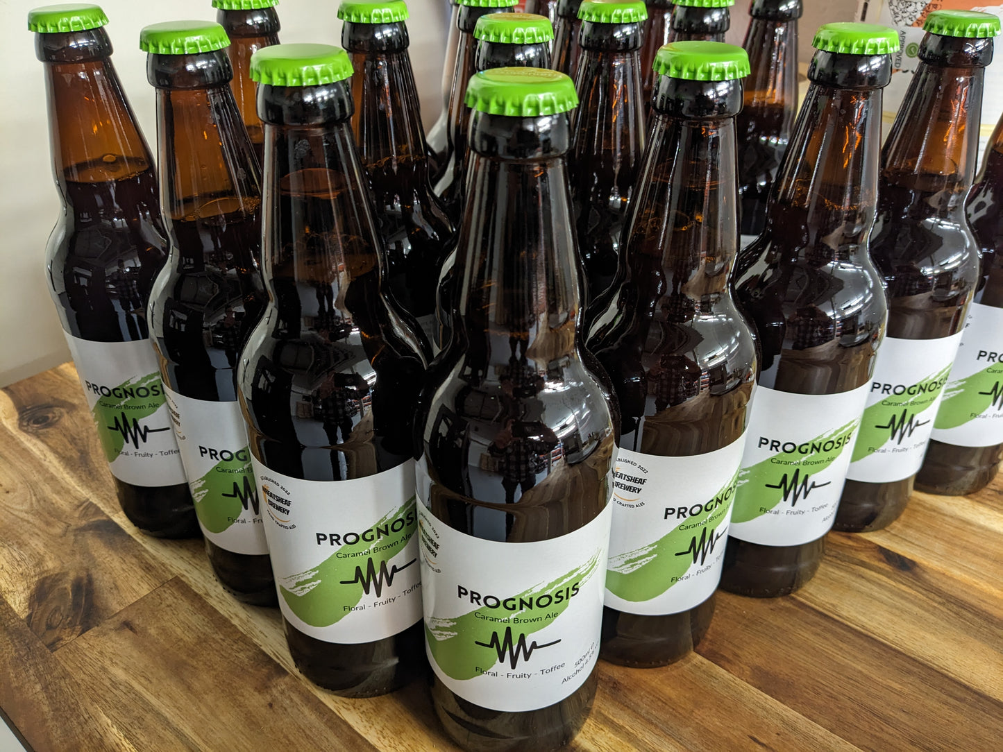 Prognosis brown ale bottles arranged in a triangle on a wooden bench. Bottle conditioned real ale brewed locally in Huntingdon, Cambridgeshire